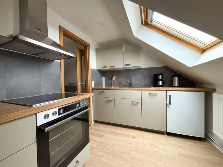 Küche Küche in der Ferienwohnung Juliane. Küchenzeile mit Herd und Ceranfeld, Dunstabzugshaube sowie Kühchrank und kleine Haushaltsgeräte.