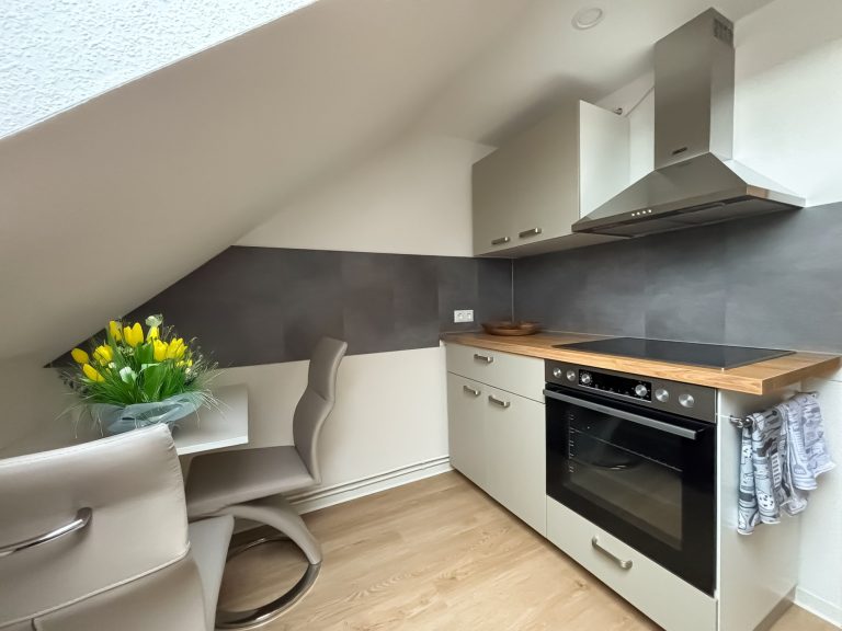 Küche Küche in der Ferienwohnung Juliane. Küchenzeile mit Herd und Ceranfeld und Dunstabzugshaube sowie ein kleiner Esstisch mit zwei Stühlen.